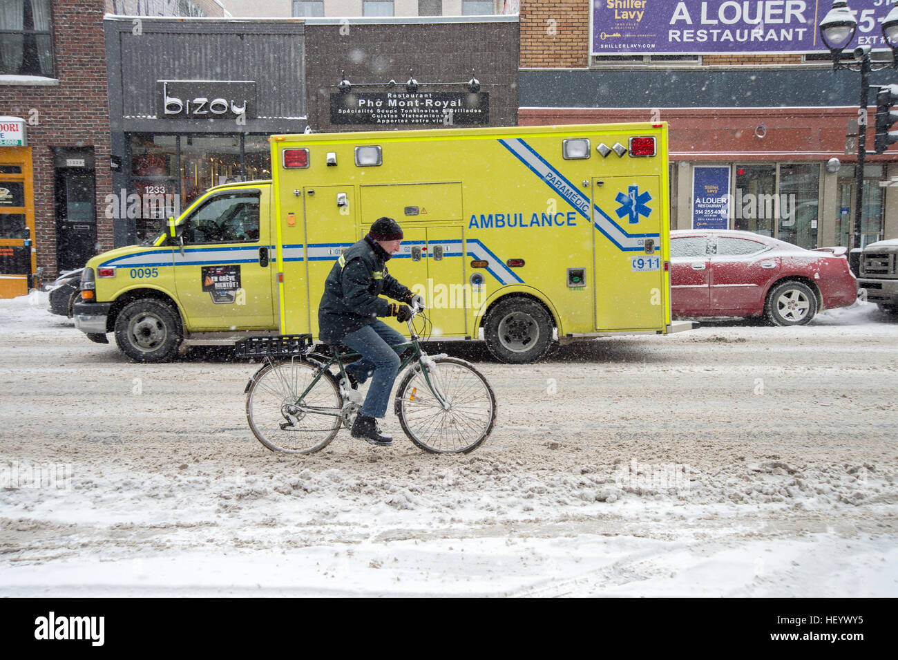 Montreal, CA, 17. Dezember 2016. Mann mit dem Fahrrad bei Schneefall in Montreal mit einem Krankenwagen im Hintergrund Stockfoto