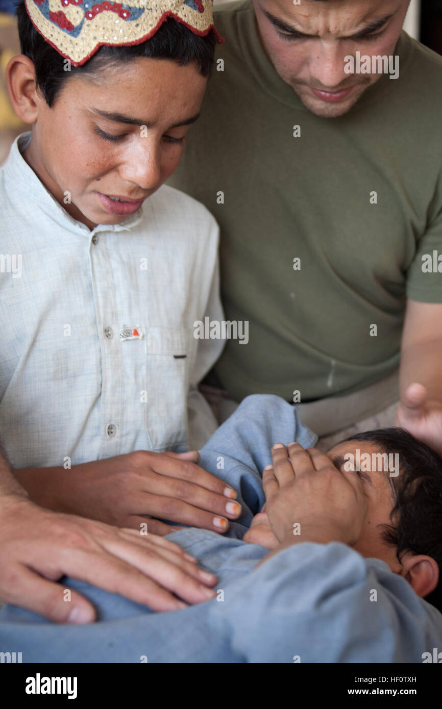 Älteren Bruder Morza, links, und Jamil, Recht, ein Linguist mit Bataillon-Hilfe-Station, 1. Bataillon, 7. Marineregiment Regimental Combat Team 6, Komfort Towuz, einem lokalen afghanischen jungen als US Navy Sanitätern Werk, eine Wunde am Bein auf Forward Operating Basis Jackson, Provinz Helmand, Afghanistan 28. Mai 2012 zu schließen. Towuz aufschneiden Bein wenn er weg von der Rückseite eines LKW während der Fahrt durch den Basar Sangin fiel. (Foto: U.S. Marine Corps Sgt. Logan W. Pierce/freigegeben) Navy Corpsman unterstützen auf FOB Jackson 120528-M-EU691-012 Stockfoto