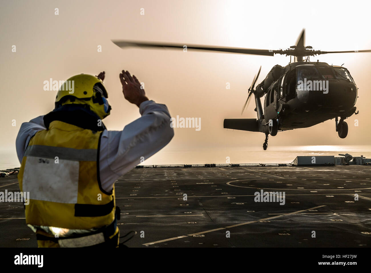 Eine Deck Hand auf die RFA Cardigan Bay, Royal Fleet Auxiliary, britische königliche Marine, gibt das Signal zum abheben, ein UH-60 medizinische Evakuierung Black Hawk von Piloten geflogen vom 1. Bataillon, 214th Air Ambulance, 42. Combat Aviation Brigade (CAB), US-Armee am 8. Juni 2014, irgendwo in den Persischen Golf.  Die Piloten ausgebildet auf Deck Landungen während Übung Spartan Kopis, einen Austausch zwischen der Cardigan Bay und die Black Hawk und AH-64 Apache Elemente der 42. Kabine, New York Army National Guard.    Spartan Kopis war das erste Mal amerikanischen Apachen mit einem Schiff der Royal Navy zu funktionieren als ich gearbeitet Stockfoto