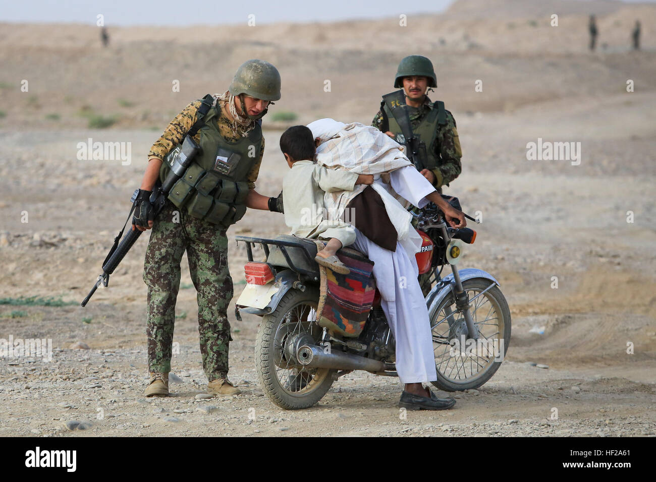 Ein Soldat von Afghan National Army (ANA), 4. Tolay, 6. Kandak, 6. Brigade 215. Korps zugewiesen hilft ein afghanische Kind eines Motorrads während der Durchführung eines Fahrzeug-Checkpoint (VCP) im Dorf Shekasteh Tappeh Provinz Helmand, Afghanistan, 14. Juli 2014. ANA-Soldaten führen VCPs um feindliche Aktivitäten zu stören, eine militärische Präsenz zu erhalten und erhöhen die Sicherheit. (Offizielle U.S. Marine Corps Foto: Lance Cpl. Darien J. Bjorndal, Marine Expeditionary Brigade Afghanistan / veröffentlicht) HELMAND-4. Tolay betreibt VCPs 140714-M-MF313-123 Stockfoto