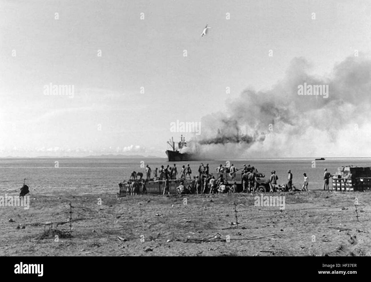 USS Alchiba (AK-23) auf Grund gelaufen und Brand vor Lunga Point, Guadalcanal, ca. Ende November 1942. Sie hatte am 28. November durch das japanische u-Boot i-16 torpediert worden. Männer sind Abfertigung am Strand, eventuell bei Entladung Alchiba, während sie ihr Feuer kämpfte. Beachten Sie Stacheldraht Fechten im Vordergrund.  US Marine Corps Foto. USS Alchiba (AK-23) auf Grund gelaufen und Brand vor Lunga Point im November 1942 Stockfoto