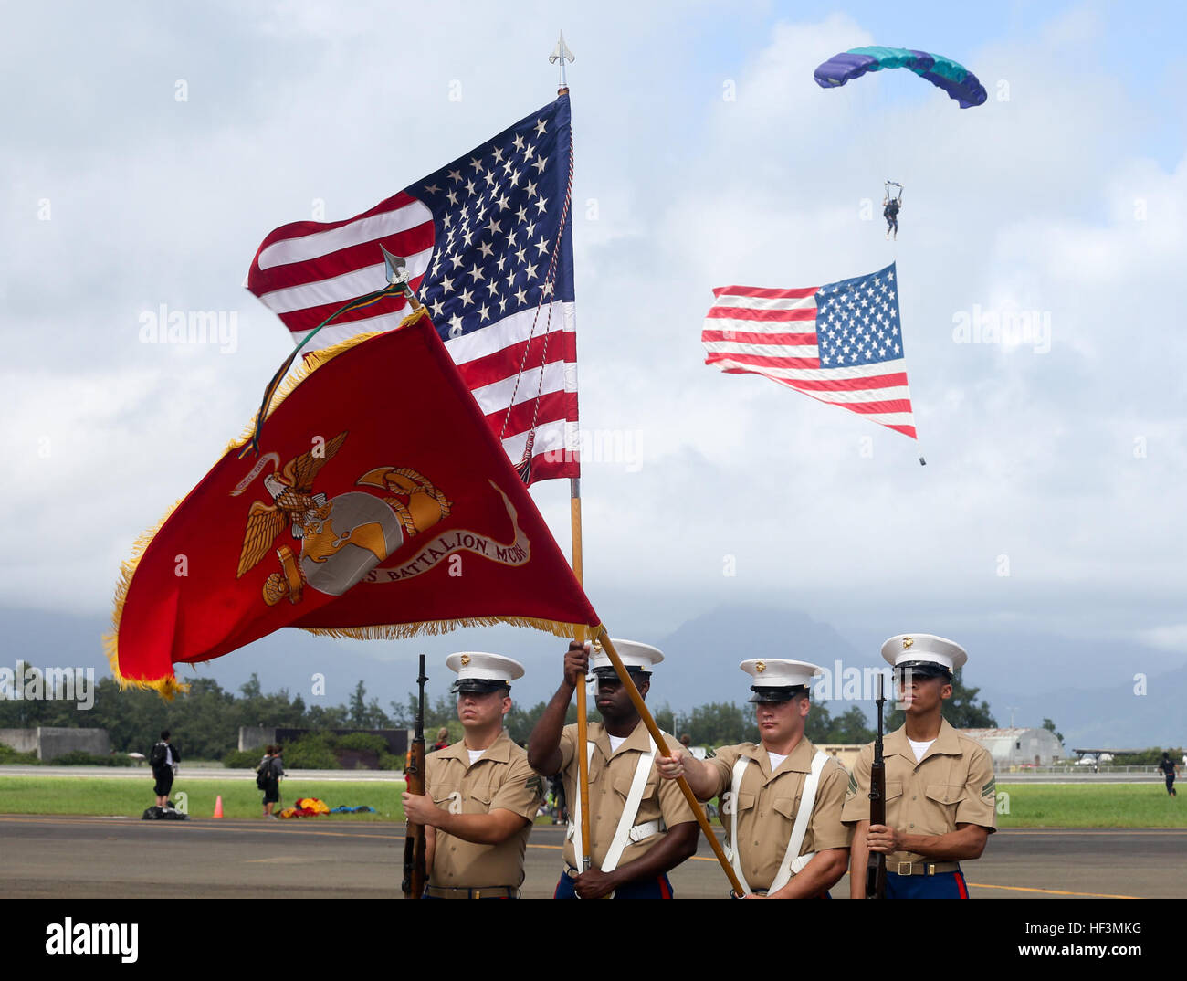 Marine Corps Base Hawaii Color Guard präsentieren Farben während der Nationalhymne als Fallschirmspringer mit der US-Flagge herabsteigt, um die Kaneohe Bay Air Show an Bord der Marine Corps Base Hawaii, 18. Oktober 2015 beginnen. Die Mission des MCB Hawaii soll Einrichtungen, Programme und Dienstleistungen zur direkten Unterstützung der Einheiten, Einzelpersonen und Familien, um zu verbessern und Kampfbereitschaft für alle operativen Kräfte unterstützen und Mieter Organisationen. (Foto: U.S. Marine Corps CPL. Ricky S. Gomez) 2015 Kaneohe Bay Airshow 151018-M-ZQ619-176 Stockfoto