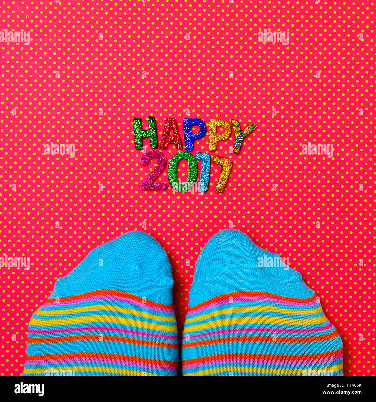 High-Angle Shot von einem Paar Füße tragen bunte gestreifte Socken und einige glitzernden Buchstaben in verschiedenen Farben bilden den Text gerne 2017, auf einem roten Stockfoto