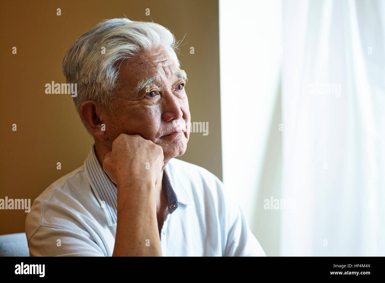 Porträt eines traurigen asiatischen senior sitzenden Menschen durch die Fenster Hand am Kinn. Stockfoto