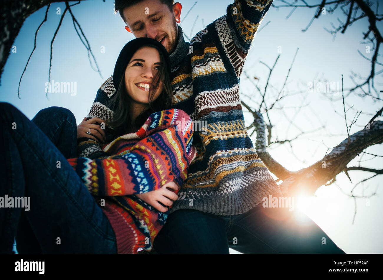 Freudige niedliche Paar umarmt. Junger Mann in einem Pullover Umarmungen ein Mädchen vom Sitzen auf Ast im Winter. Das Konzept einer erfolgreichen Beziehung und ha Stockfoto