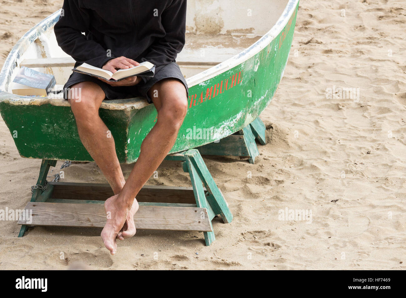 Mann liest ein Buch auf Fischerboot am Strand sitzen Stockfoto