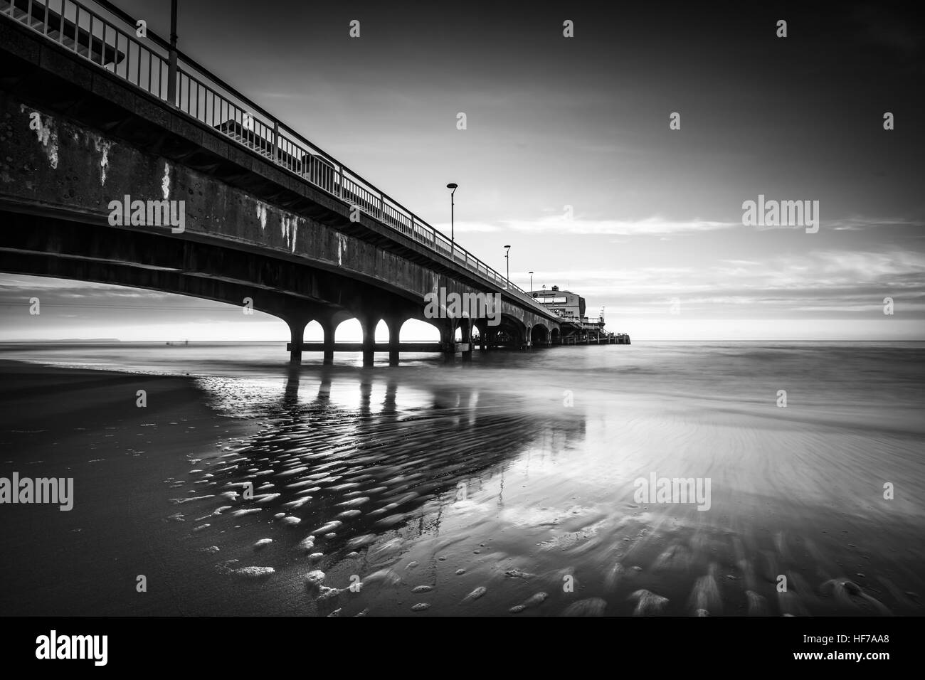 Schwarz / weiß Bild von Bournemouth Pier mit Reflexionen des Sonnenaufgangs im Wasser Stockfoto