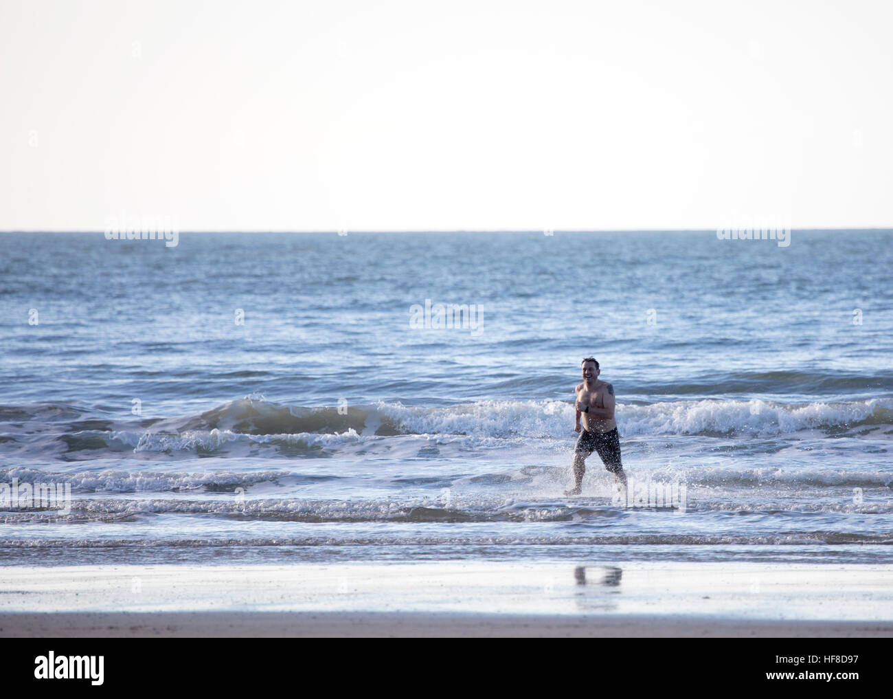 Ein Mann läuft aus dem Meer nach dem Bad bei Newborough Strand, Wales, UK während Frühlingssonne Stockfoto