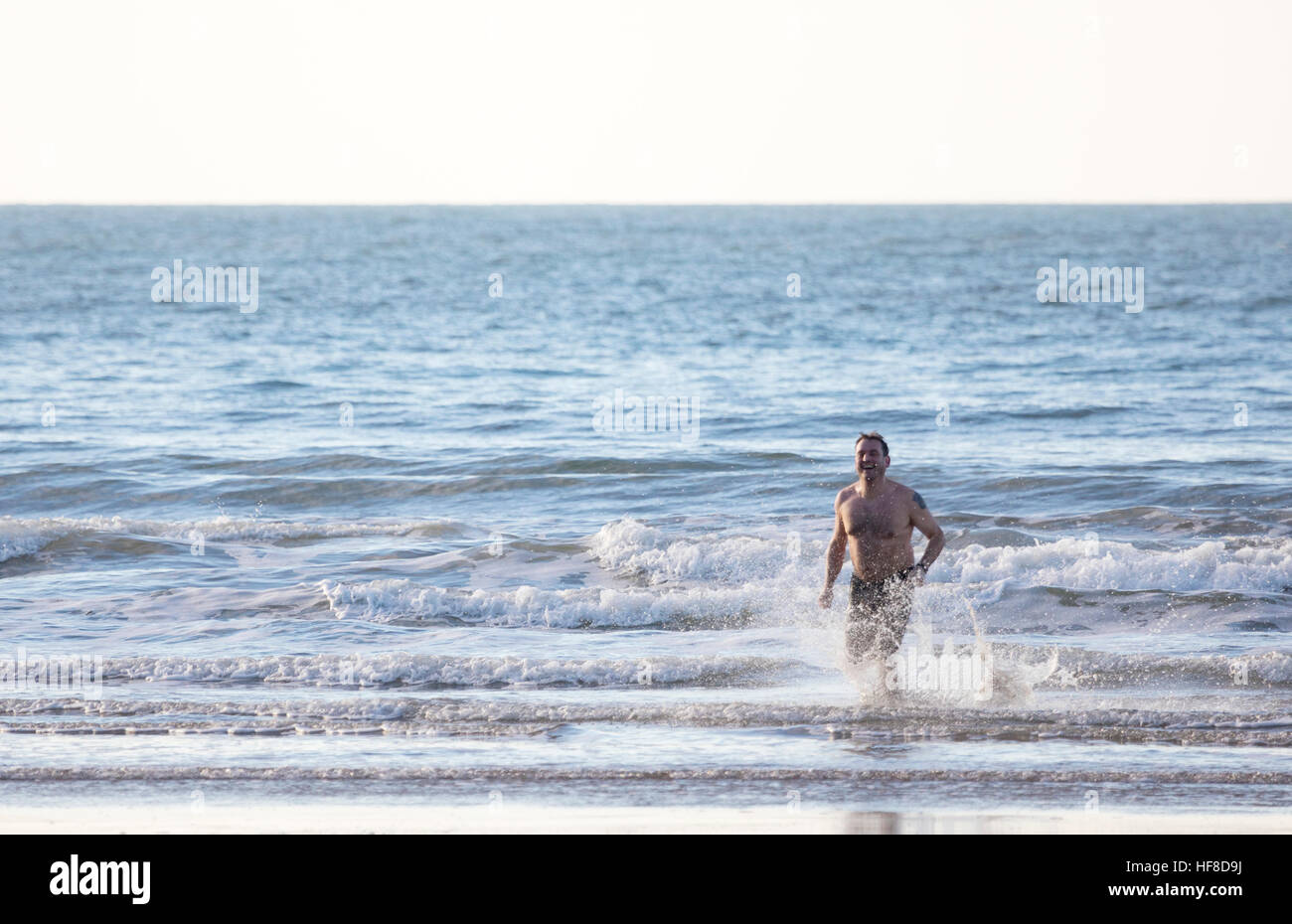 Ein Mann läuft aus dem Meer nach dem Bad bei Newborough Strand, Wales, UK während Frühlingssonne Stockfoto