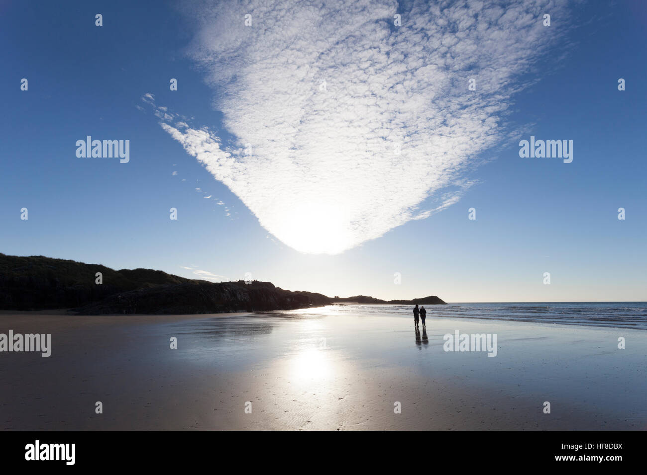 Ein paar wenige entlang einer ruhigen unberührten Strand in Aldeburgh Strand mit Ynys Llanddwyn oder llanddwyn Island in der Ferne, Anglesey, Wales, Großbritannien Stockfoto