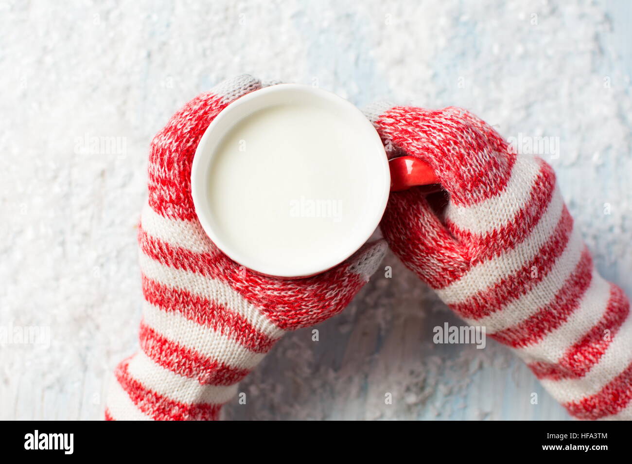 weibliche Hände in Handschuhe halten heiße Tasse Milch über einen verschneiten Hintergrund Stockfoto