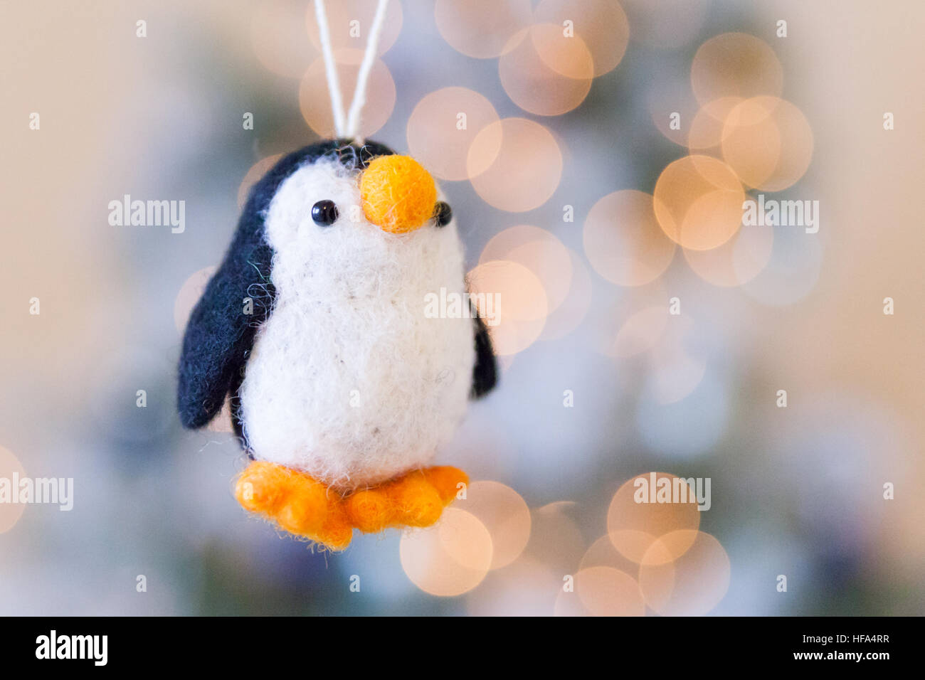 Schwarz / weiß Filz Pinguin Weihnachtsbaum Dekoration mit Lichterkette Bokeh in Orange und blau. Weihnachtszeit Stockfoto