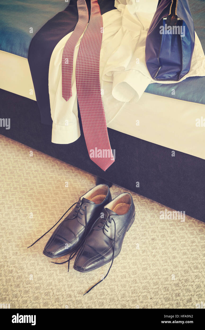 Retro-stilisierte männliche Schwarze Lederschuhe und Kleidung auf einem Hotel-Zimmer-Bett. Stockfoto