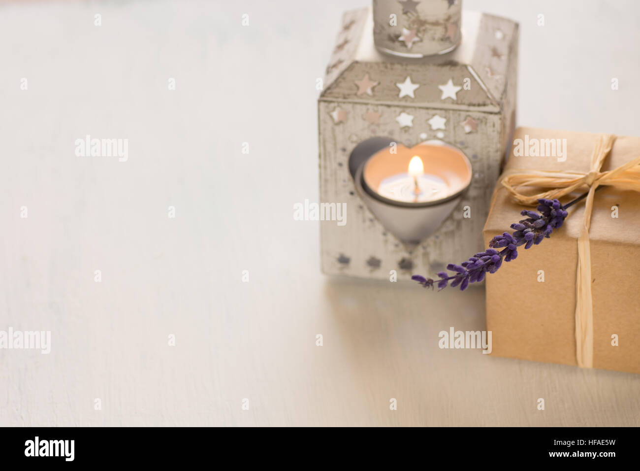 Geschenkbox mit einem Lavendel Zweig, herzförmige Kerze-Halter mit brennendem Teelicht auf weißem Hintergrund in Contre jour Stockfoto