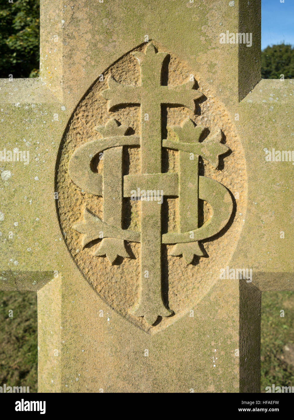 Nahaufnahme Detail geschnitzten IHS-Monogramm auf einem Sandstein Grabstein Kreuz Rasen und Bäumen im Hintergrund Stockfoto