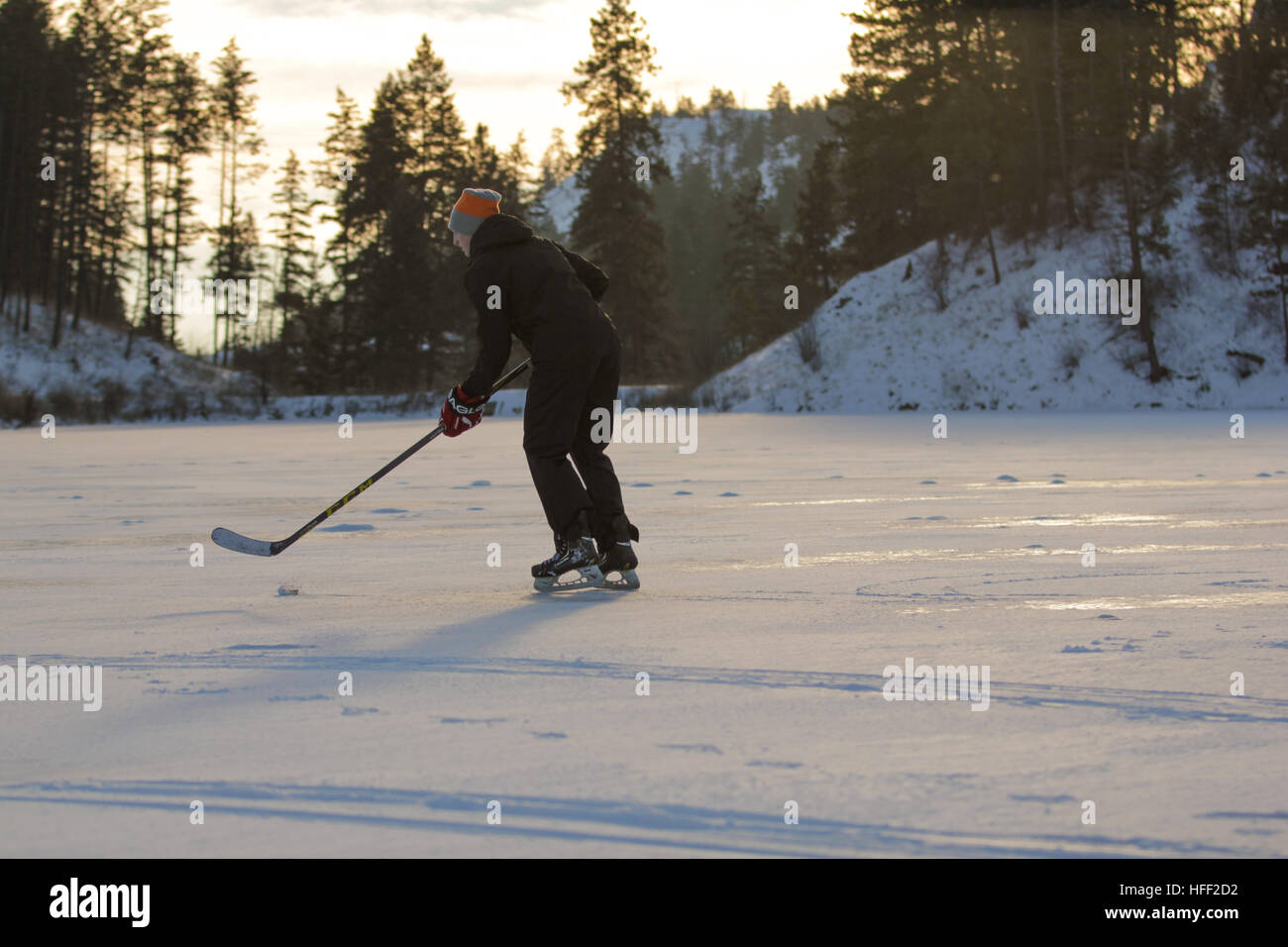Kanadischer Teenager, der an einem sonnigen, aber kalten Winternachmittag auf einem gefrorenen See Schlittschuh läuft und Eishockey spielt Stockfoto