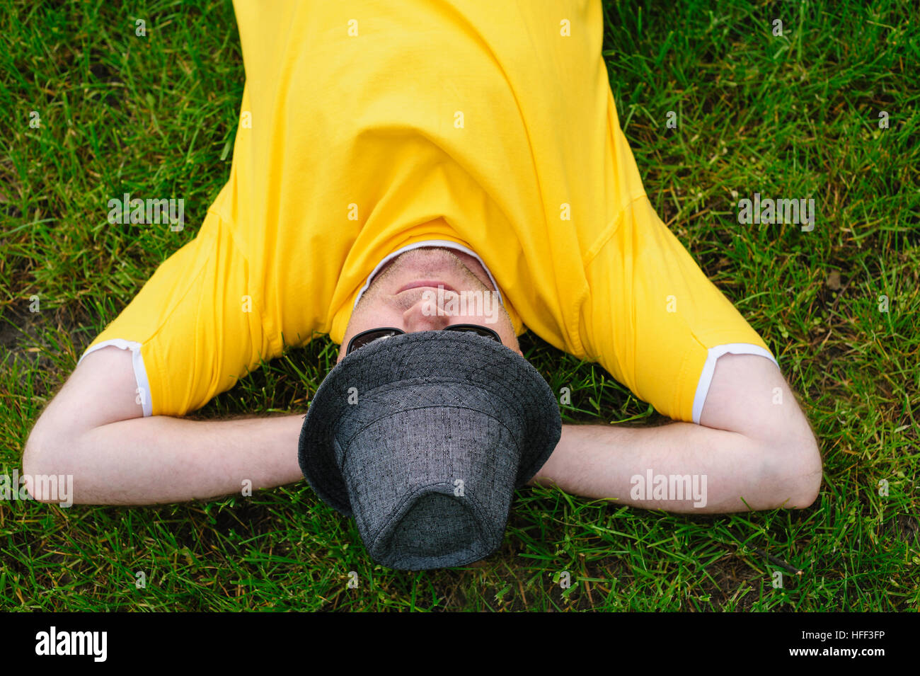 Mann im gelben T-shirt und Hut auf dem Rasen liegend Stockfoto