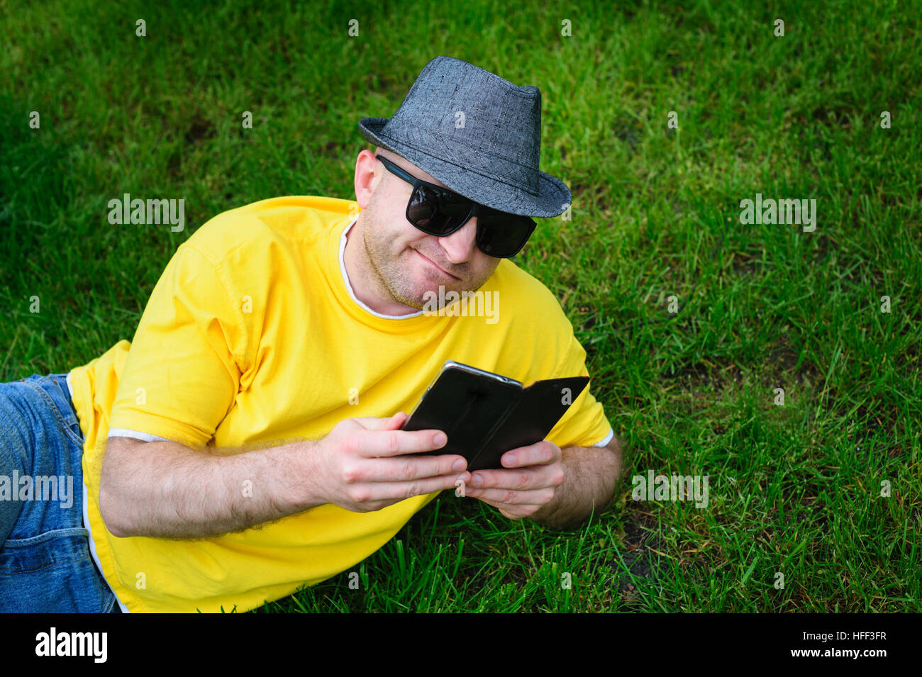Mann mit Hut liegen auf dem Rasen und Telefon Stockfoto