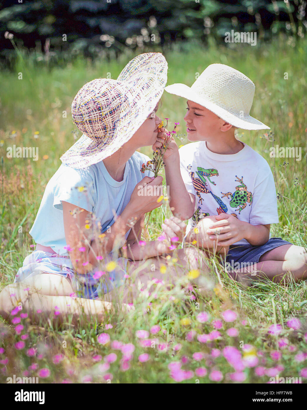 Glückliche Kinder, ein Junge und ein Mädchen, im Stroh Hüte sitzen in einem Feld riechen Wildblumen. Stockfoto
