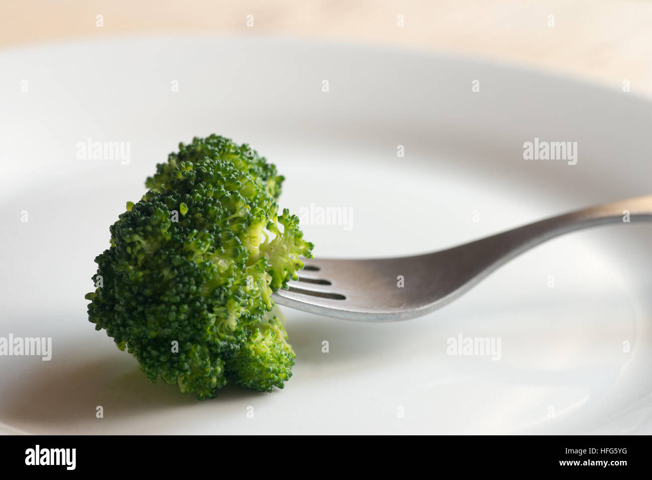 Stück Brokkoli auf Gabel auf weißen Teller Stockfoto