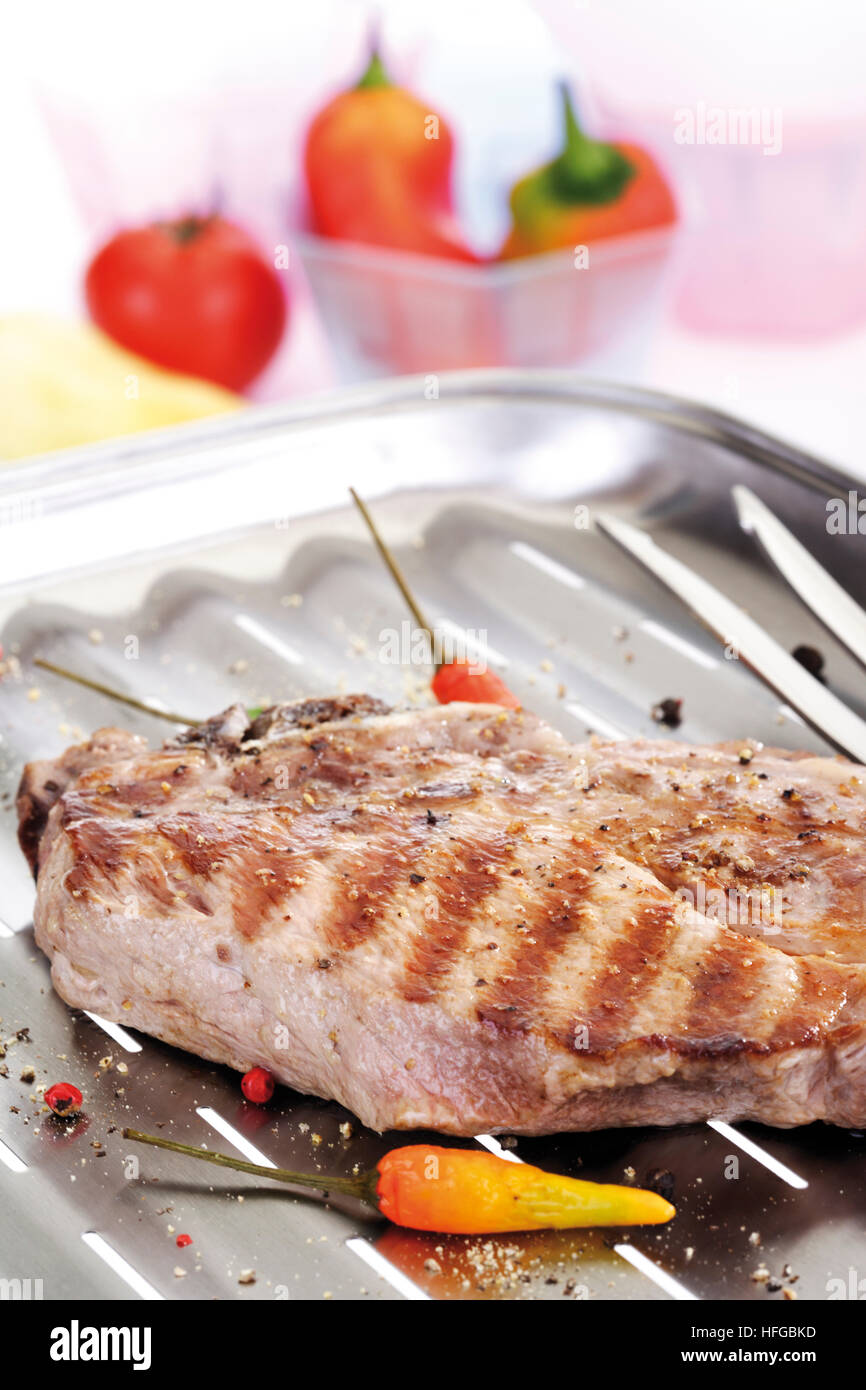 Gegrilltes Schweineschnitzel, Grill-Marken auf eine Aluminium-Grill mit Fleischgabel, Schüssel mit Paprika im Hintergrund Stockfoto