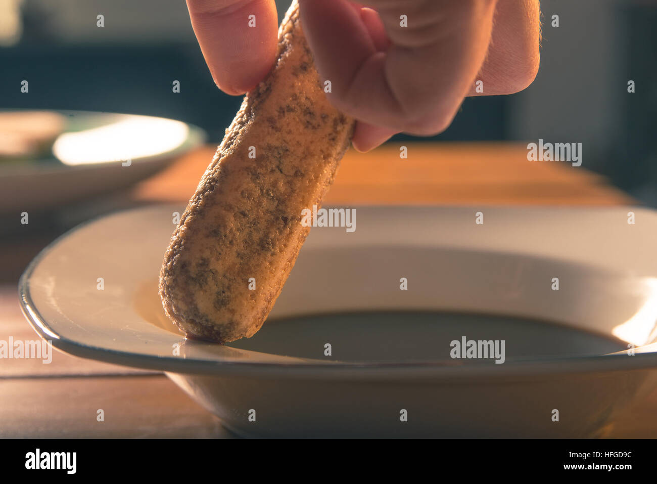 Hand taucht ein Savoiardi Biskuit in Kaffee Stockfoto