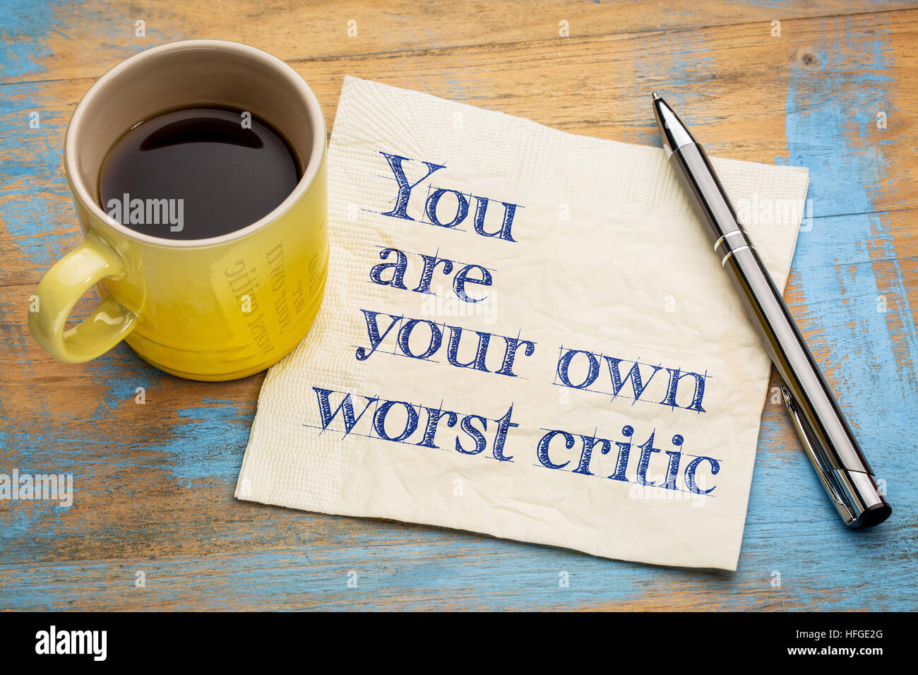 Sie werden Ihre eigenen schlimmsten Kritiker - Handschrift auf einer Serviette mit einer Tasse Espressokaffee Stockfoto