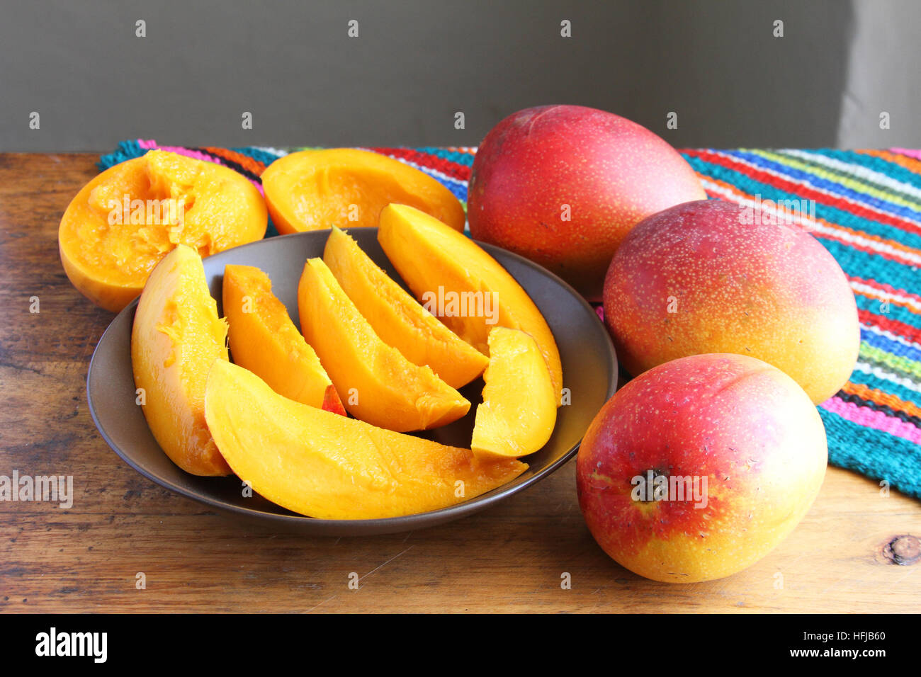 Bunte ganze und geschnittene Mangos auf Holztisch mit farbenfrohen Tischset Stockfoto