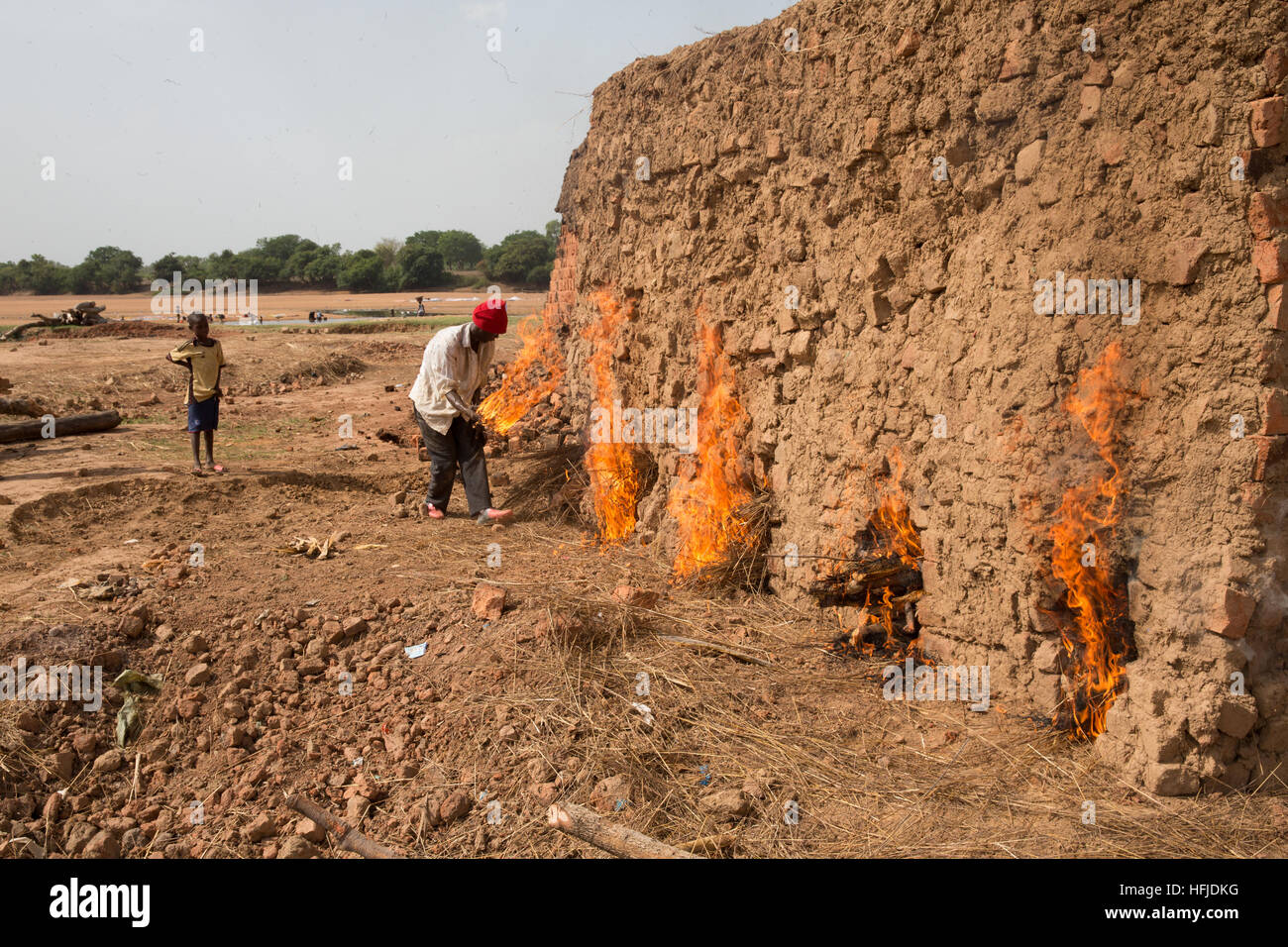Kiniero, Guinea, 30. April 2015: Mory Condé, 30 Jahre alt, legt Holz steigen Sie unter seinem Stein Ofen seine Steine abzufeuern. Stockfoto