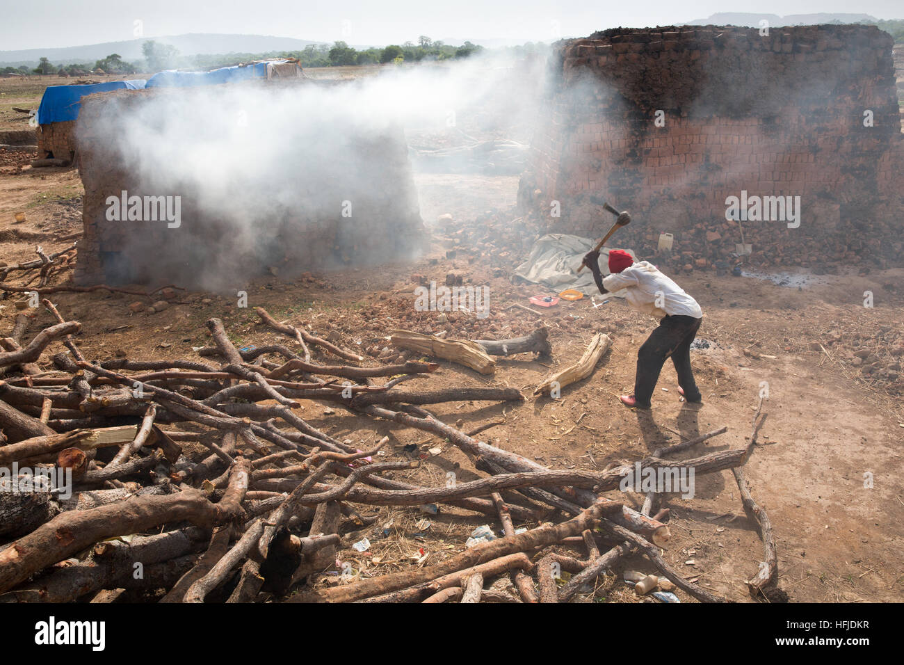 Kiniero, Guinea, 30. April 2015: Mory Condé, 30 Jahre alt, legt Holz steigen Sie unter seinem Stein Ofen seine Steine abzufeuern. Stockfoto