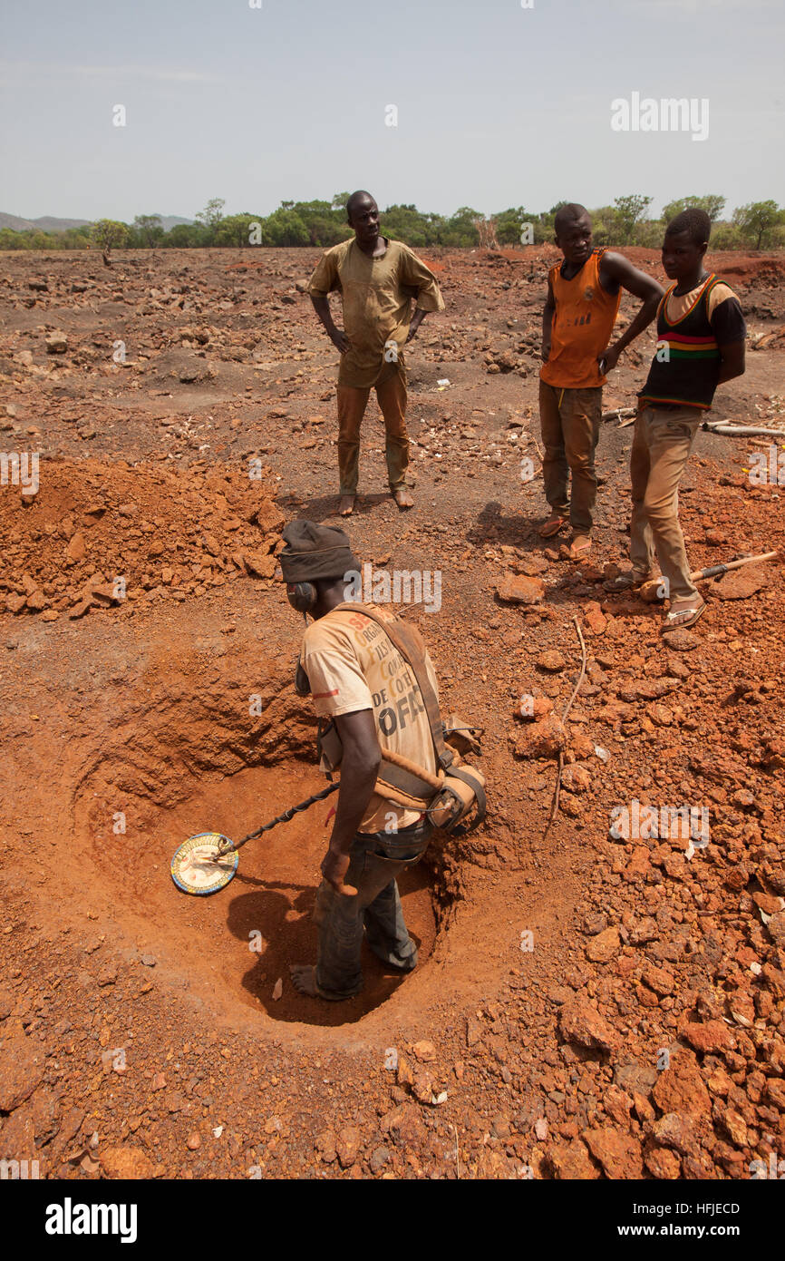 Sanana Goldmine, Guinea, 2. Mai 2015; Bergleute graben, während andere ein Mann mit einem Metalldetektor ihre Masse prüfen. Stockfoto