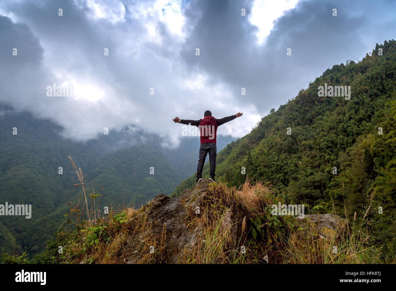 Mann öffnet seine Arme mit Blick auf eine lebendige nebligen Himmel stehend auf einem Hügel in der Nähe von Chungthang in Nord-Sikkim, Indien. Stockfoto