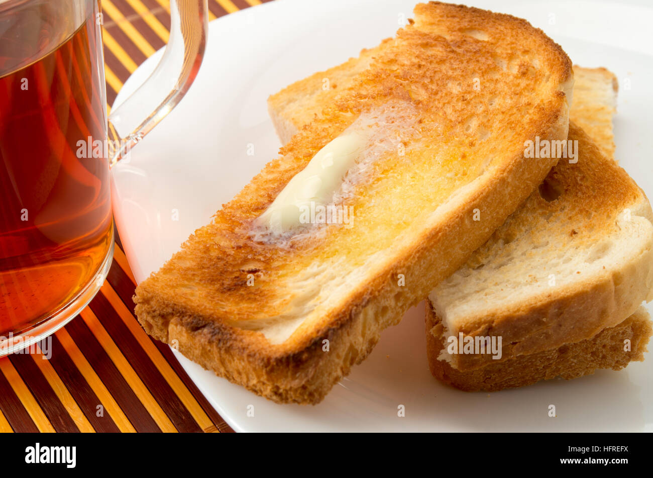 Warmen Toast mit Butter auf einem weißen Teller und eine transparente Tasse Tee closeup Stockfoto