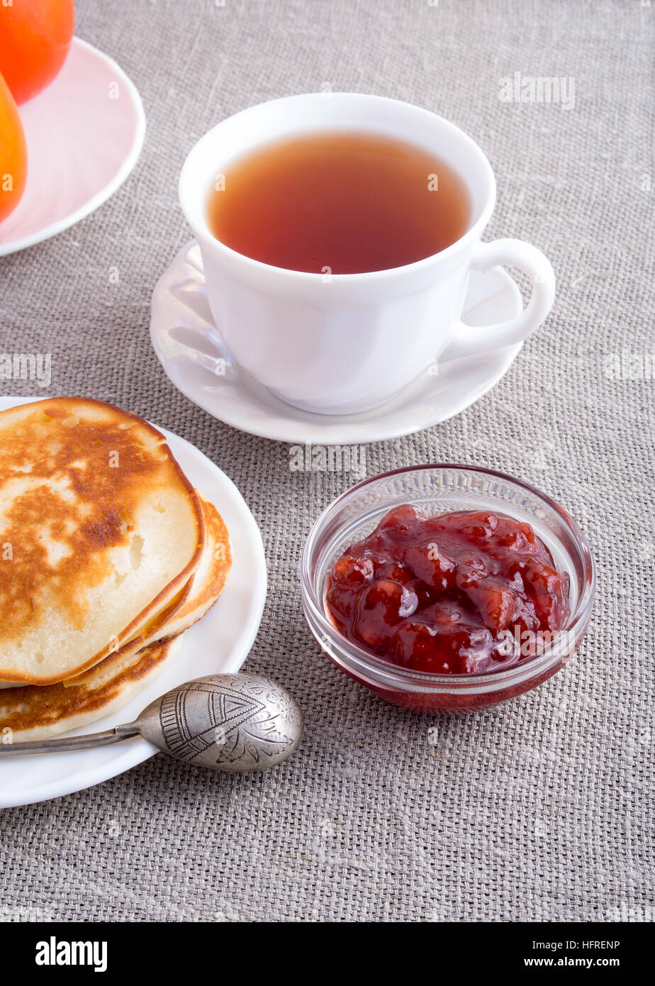 Ein Teller mit heißen Pfannkuchen mit Vintage Silber Löffel, eine Tasse Tee und eine Glasschale mit Erdbeer-Marmelade auf einem grauen Textil-Hintergrund Stockfoto