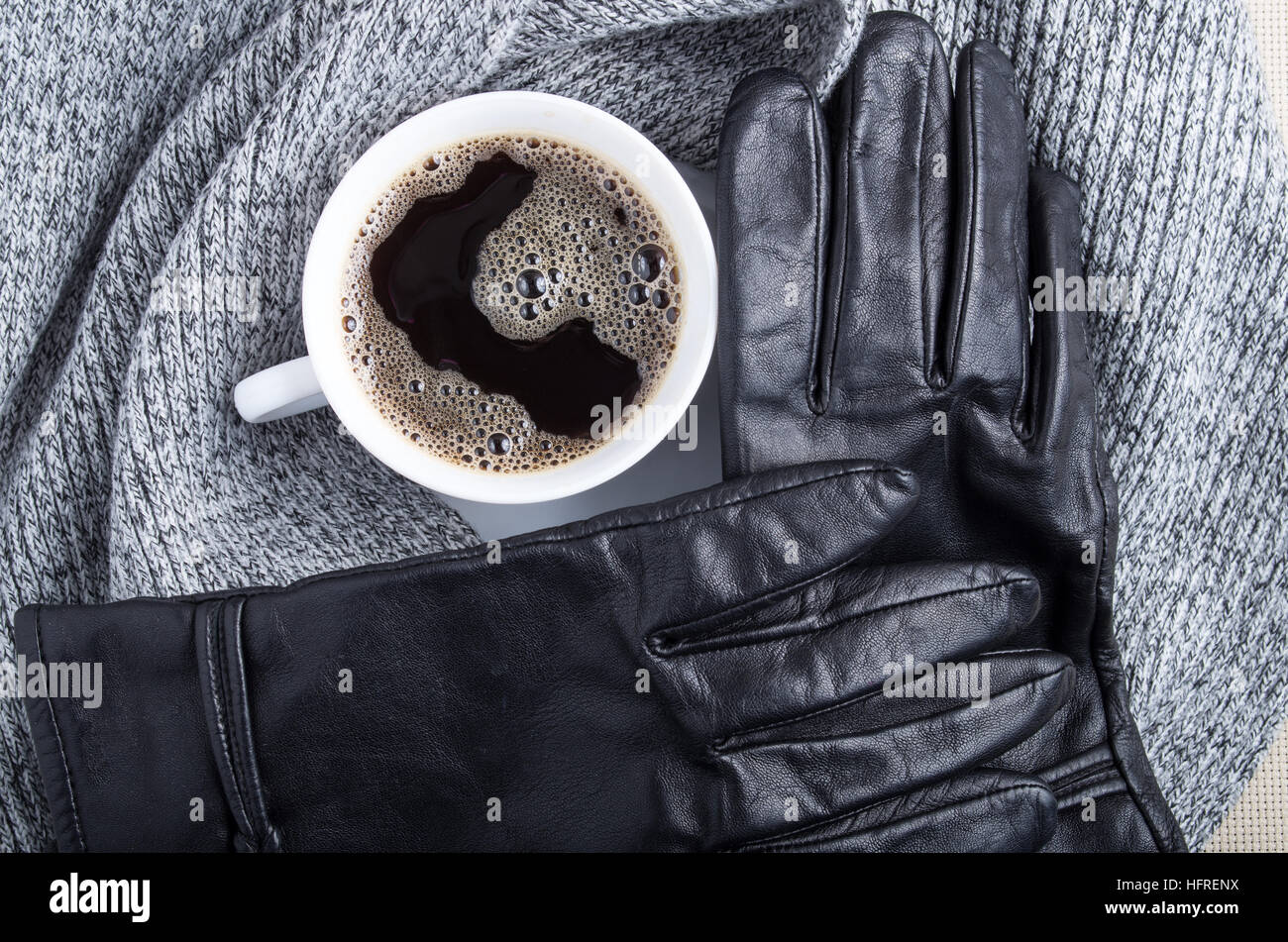 Draufsicht auf eine weiße Tasse Kaffee, einen grauen Schal und schwarze Handschuhe sind aus Leder gefertigt Stockfoto