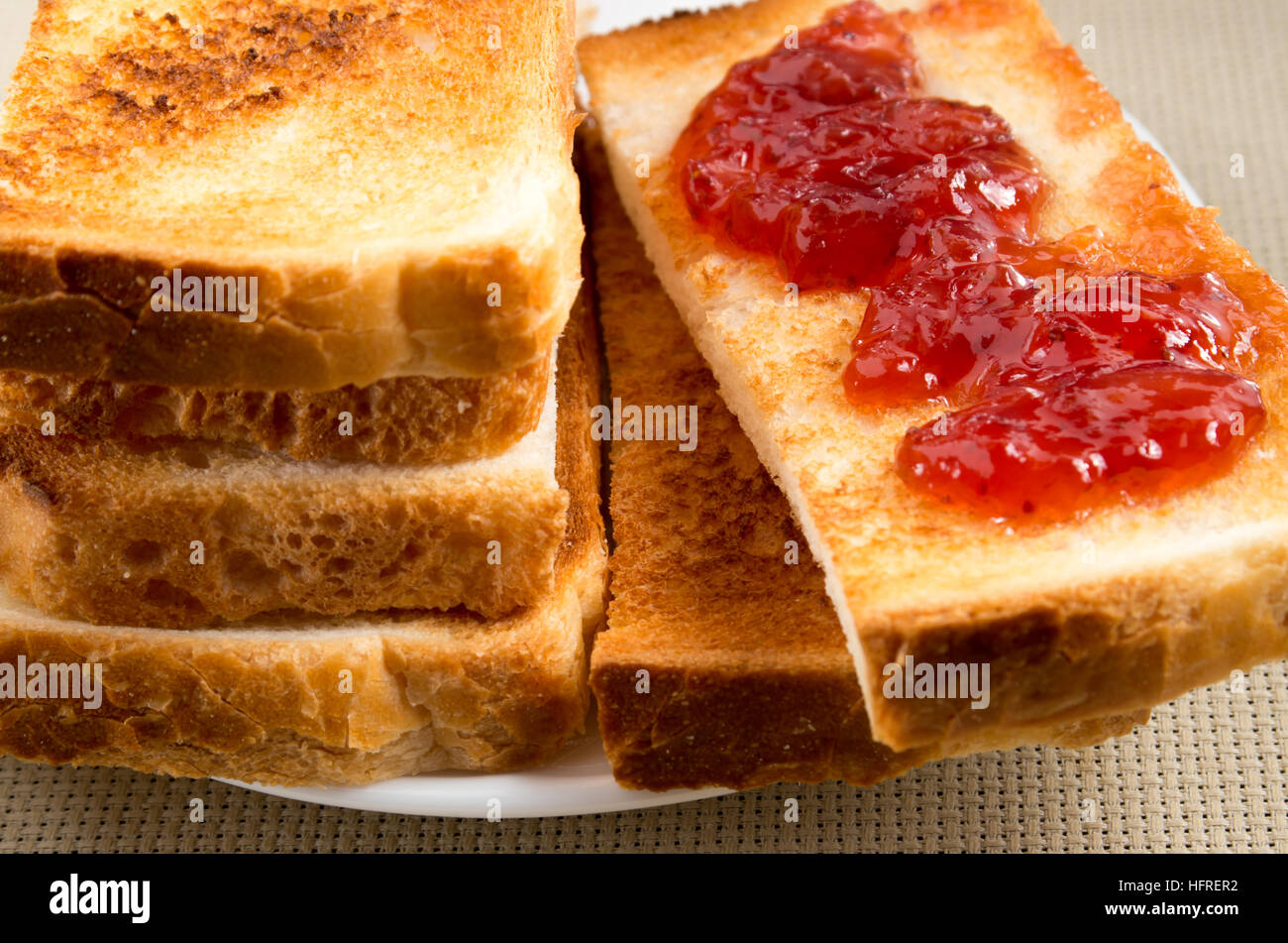 Geröstete Brotscheiben mit Strawberry jam close-up auf einem Tisch mit Geschirr und der Hintergrund jedoch unscharf Stockfoto