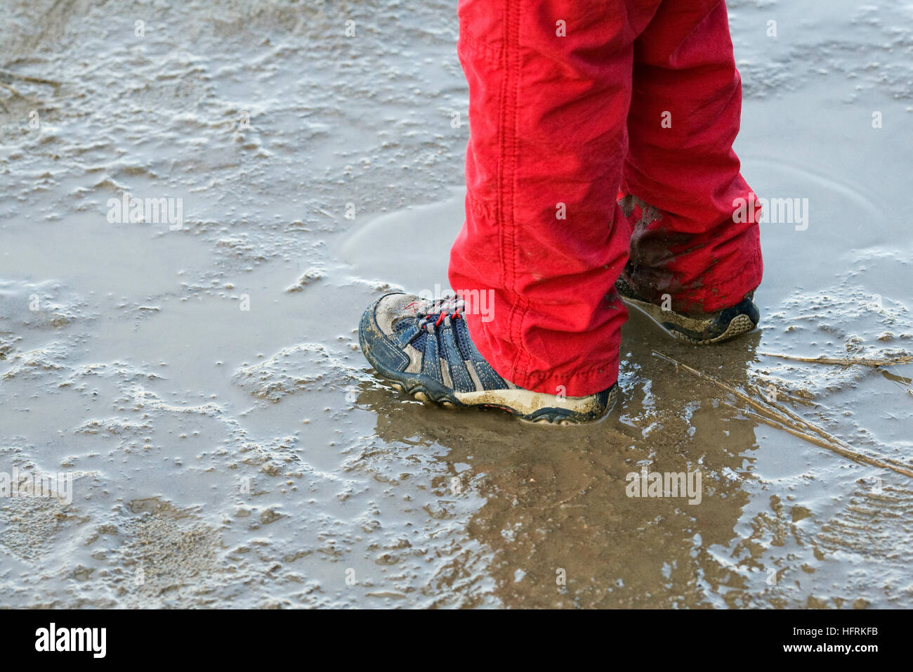 Ein kleines Kind in einer schlammigen Pfütze spielen. Stockfoto