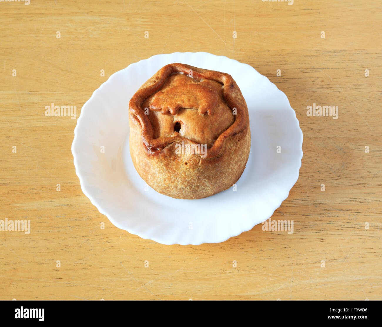 Ein Melton Mowbray Pork Pie auf einem weißen Teller auf einem Holztisch. Stockfoto