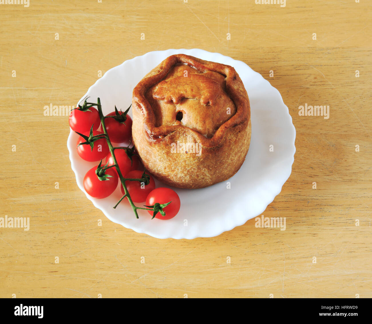 Ein Melton Mowbray Pork Pie auf einem weißen Teller mit Cherry-Tomaten. Stockfoto