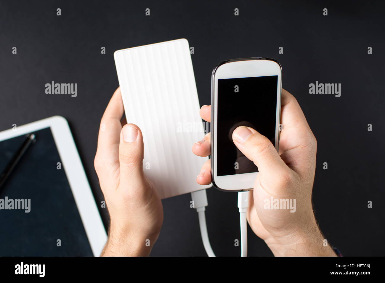 männliche Hände halten ein weißes Handy verbunden, eine Powerbank auf schwarz Stockfoto