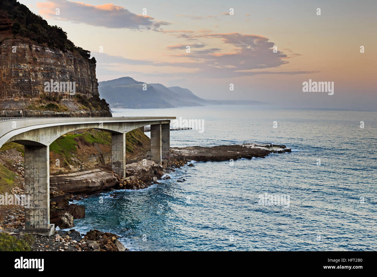 Seitenansicht der Sea Cliff Bridge auf Grand Pacific Drive in Australien. Hellen Sonnenuntergang über Pazifischen Ozean von malerischen Tourismus motor hin gerichteten hügeligen Küste. Stockfoto