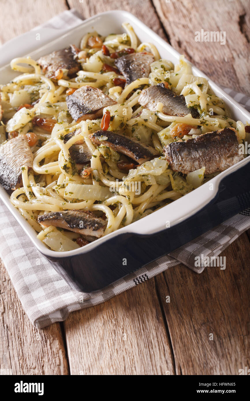 Italienische Küche: Pasta mit Sardinen, Fenchel, Rosinen und Pinienkernen hautnah in Auflaufform auf den Tisch. vertikale Stockfoto