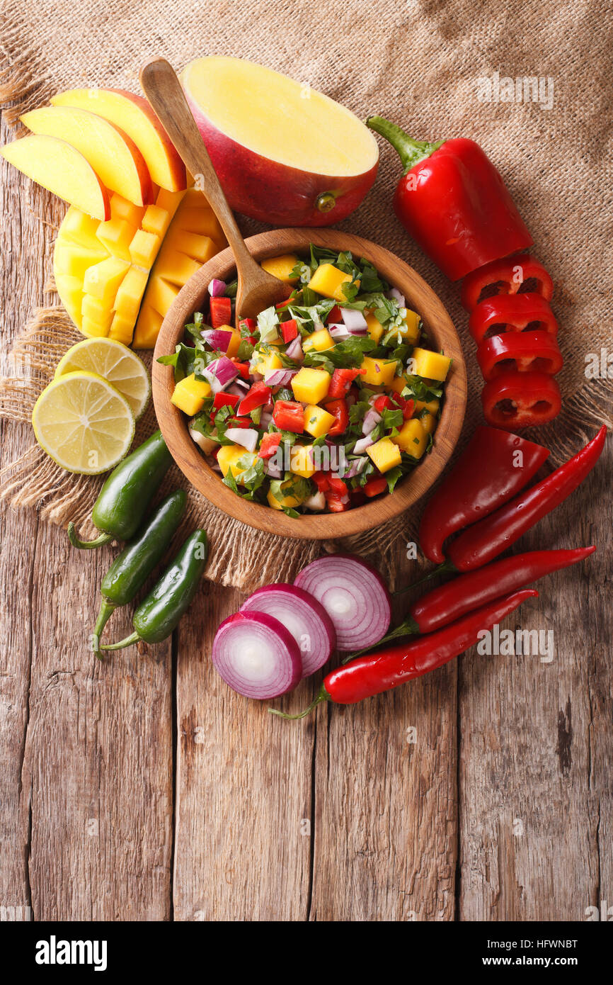 Mexikanisches Essen: Salsa mit Mango, Koriander, Zwiebeln und Paprika hautnah in eine Schüssel geben und die Zutaten auf den Tisch. vertikale Ansicht von oben Stockfoto