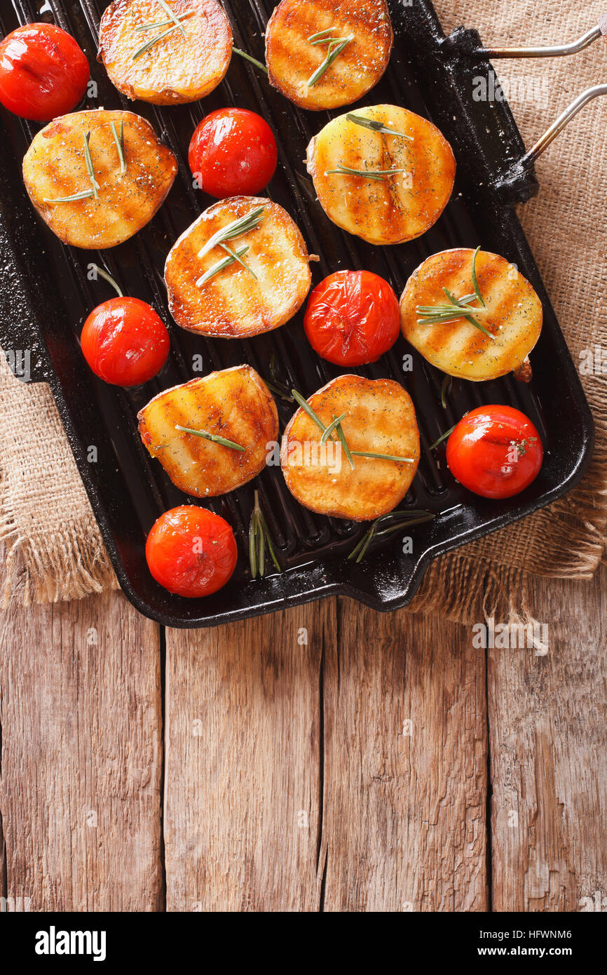 Lecker gebratene Kartoffeln und Tomaten mit Rosmarin hautnah auf einer Grillpfanne. vertikale Ansicht von oben Stockfoto