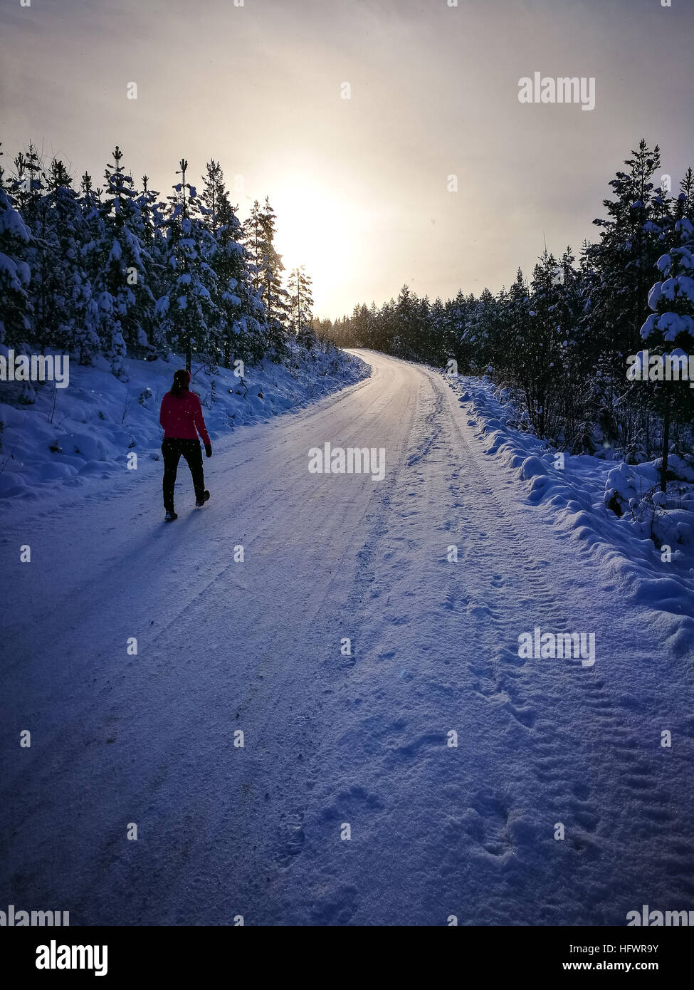 Frau zu Fuß in Sonnenuntergang im Winter auf verschneiten Straßen. Lange Schatten. Stockfoto