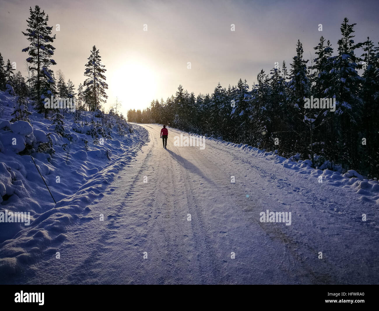 Frau zu Fuß in Sonnenuntergang im Winter auf verschneiten Straßen. Lange Schatten. Stockfoto