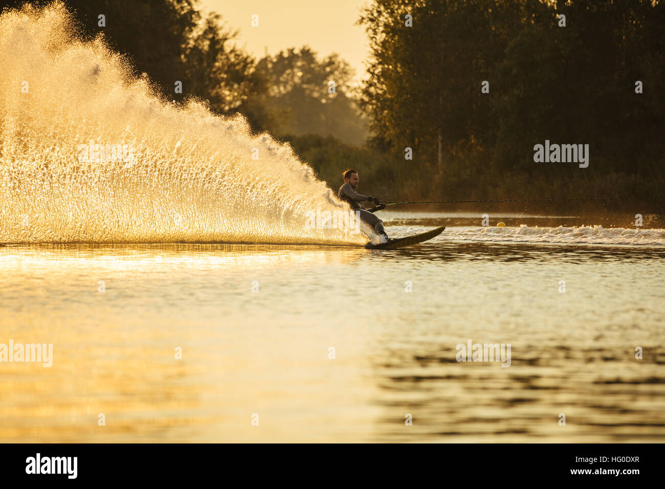 Mann reitet Wakeboard auf See mit Spritzwasser. Man Wasserski bei Sonnenuntergang. Stockfoto