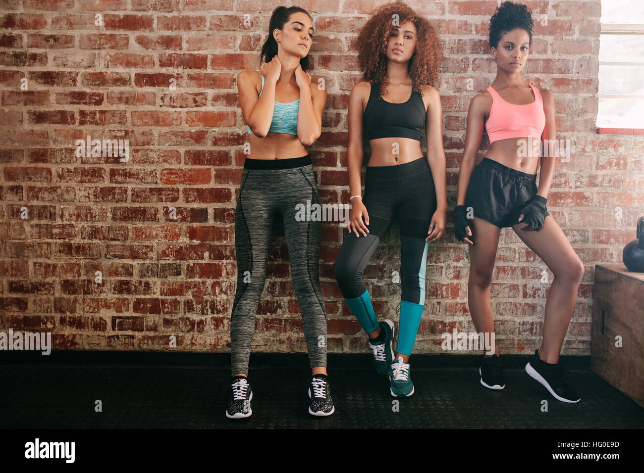 Porträt von Fitness Frauen in Sportbekleidung stehend gegen Ziegel Wand in Fitness-Studio. Gemischtrassigen Gruppe von Frauen zusammen stehen im Fitnessraum. Stockfoto