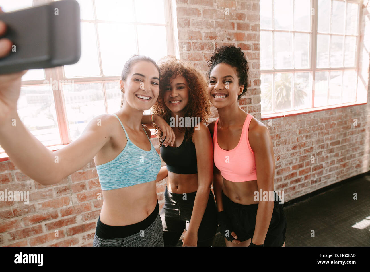 Gruppe der glückliche junge Frauen, die die Selfie per Smartphone im Fitness-Studio. Gemischtrassigen Gruppe von Mädchen im Fitnessraum unter Selbstporträt in Pause. Stockfoto