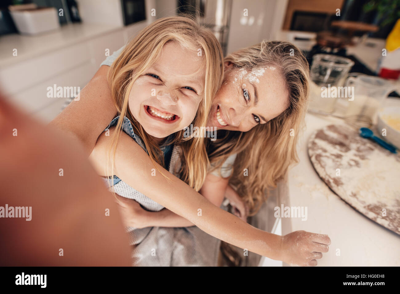 Lächelnde Mädchen und Frau in der Küche nehmen Selfie. Glückliche junge Mutter und Tochter kochen. Stockfoto